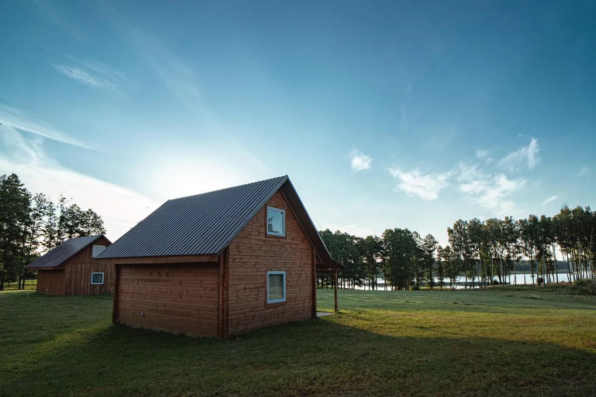 Namelio miegamasis — patogioji lova, grazus šviesa iš langų, ramų gamtos scena