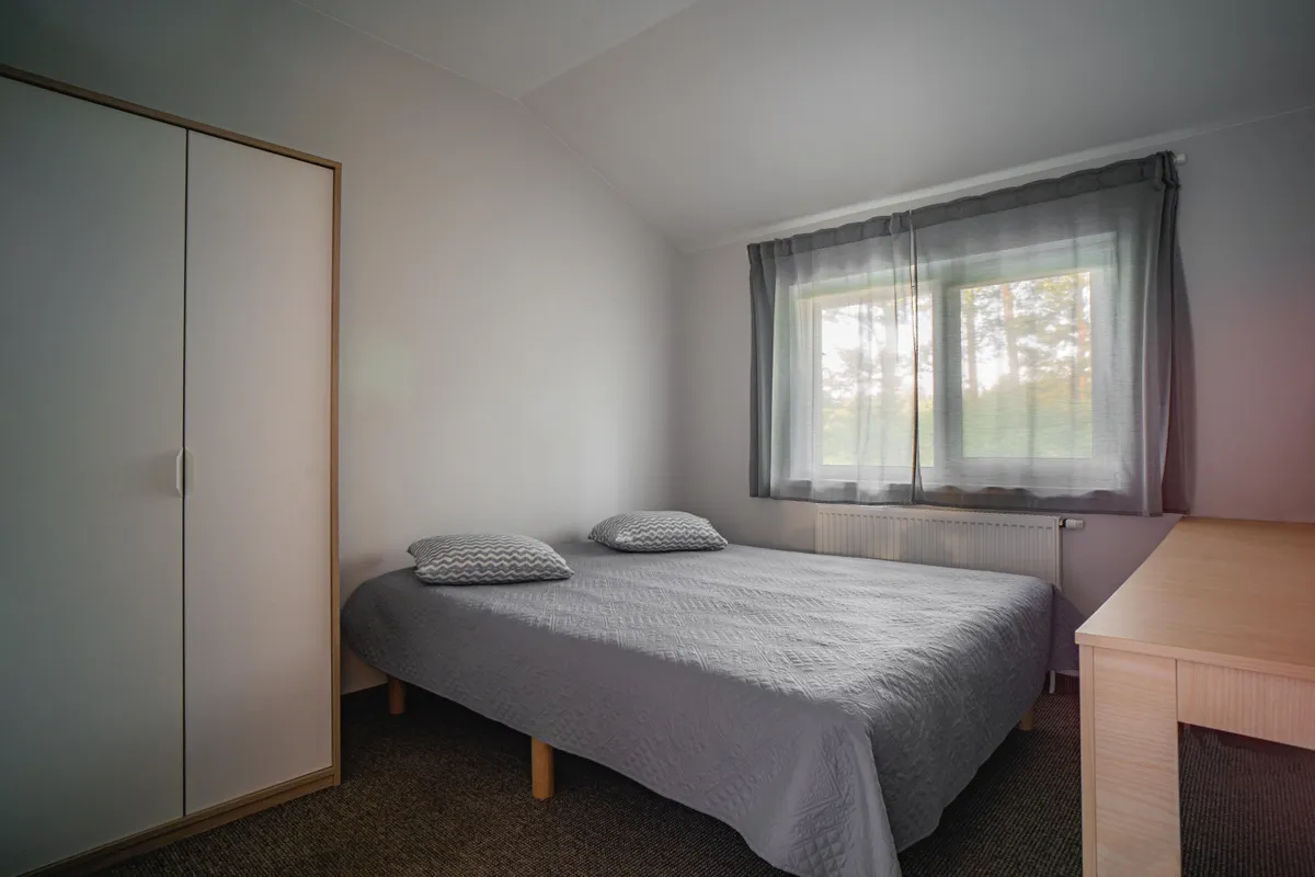 Miegamasis — didelė patogioji lova, gamtos spalvos tekstilės, langas į mišką